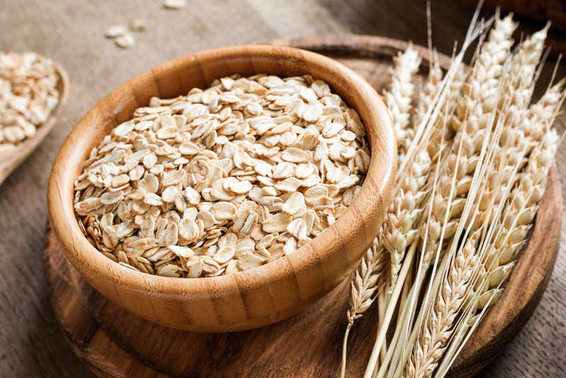 Rolled oats or oat flakes and golden wheat ears on wooden background.